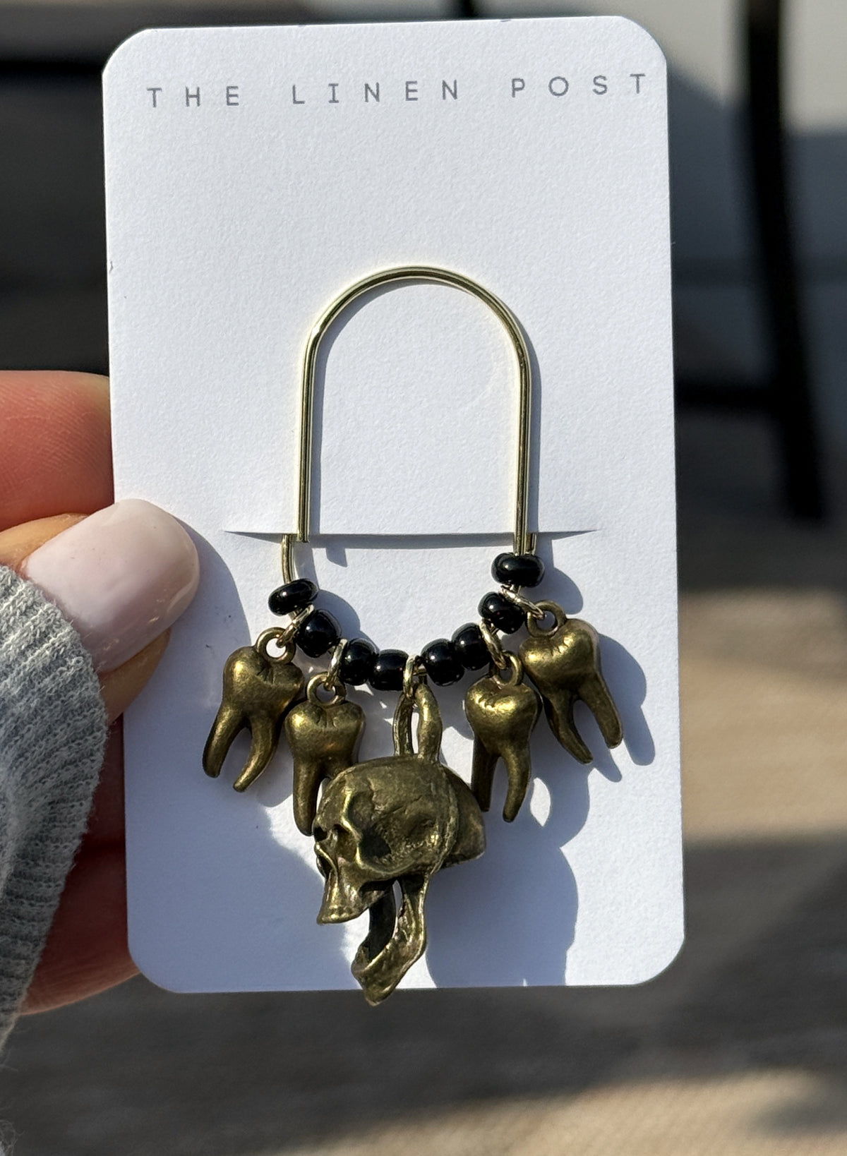 Bronze Skull & Teeth Planner Clip on its card, held in hand